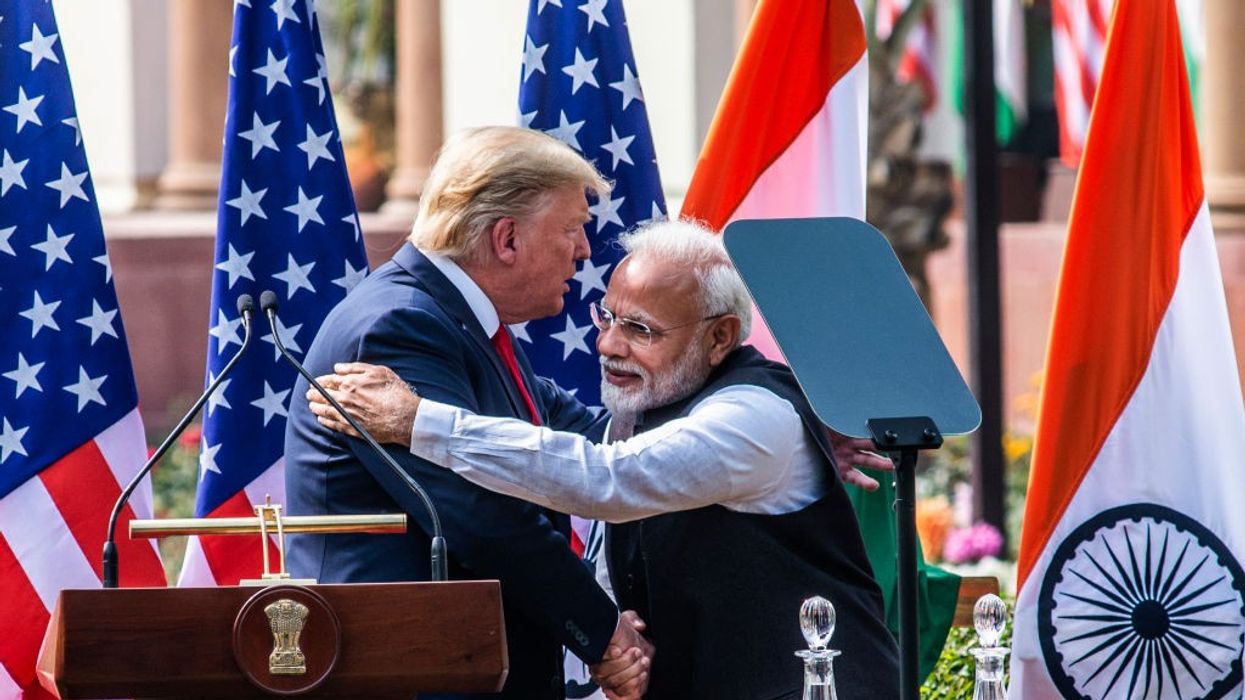 Two men embrace and shake hands in front of flags.