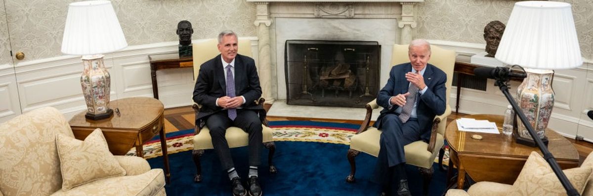 Two men in suits sit in chairs. 
