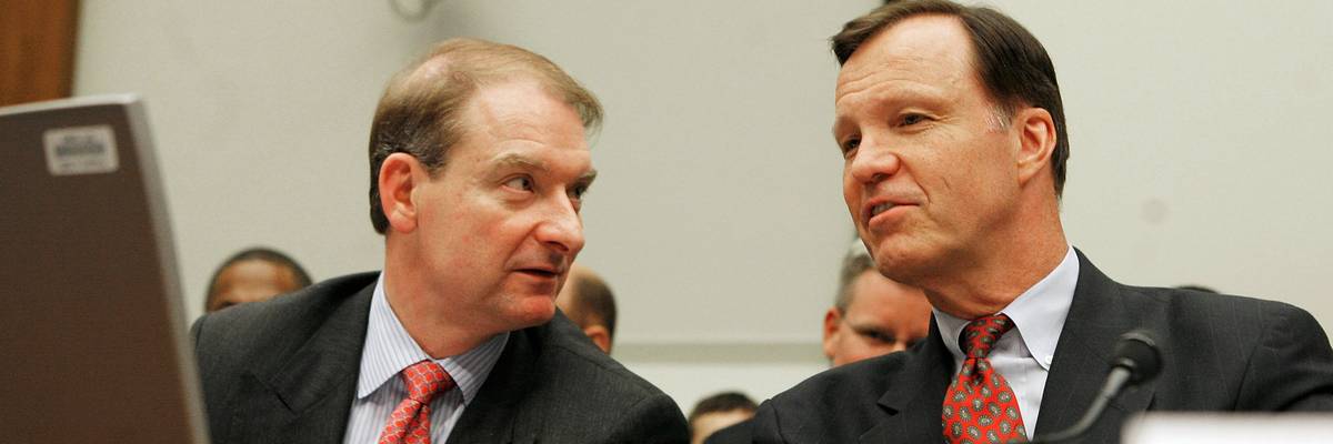 Two men in suits speak to one another.