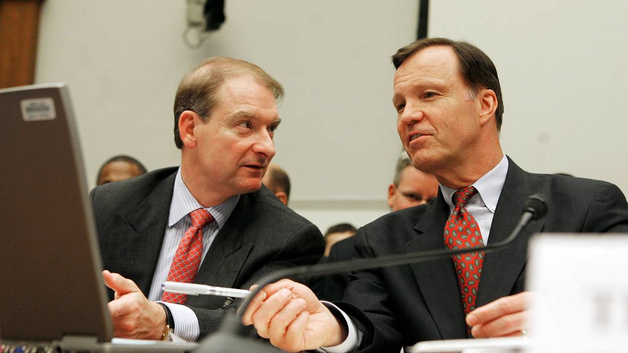 Two men in suits speak to one another.