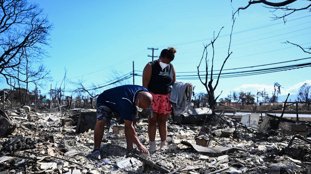 Two poeple look through the ashes of their home in Maui