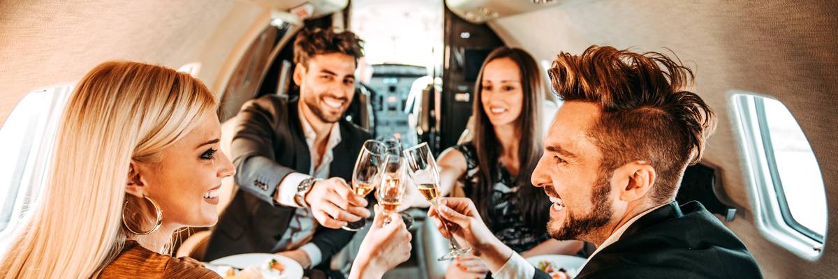 Two rich couples putting their glasses together in a celebratory toast while traveling on a private airplane