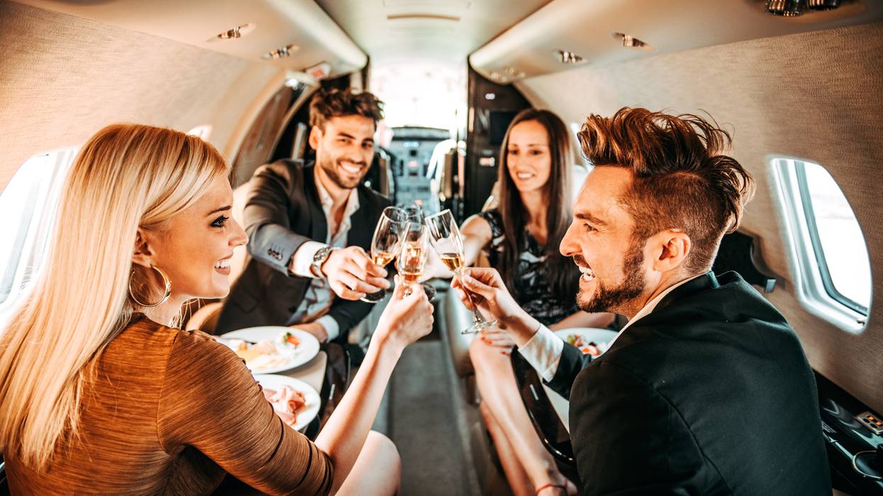 Two rich couples putting their glasses together in a celebratory toast while traveling on a private airplane