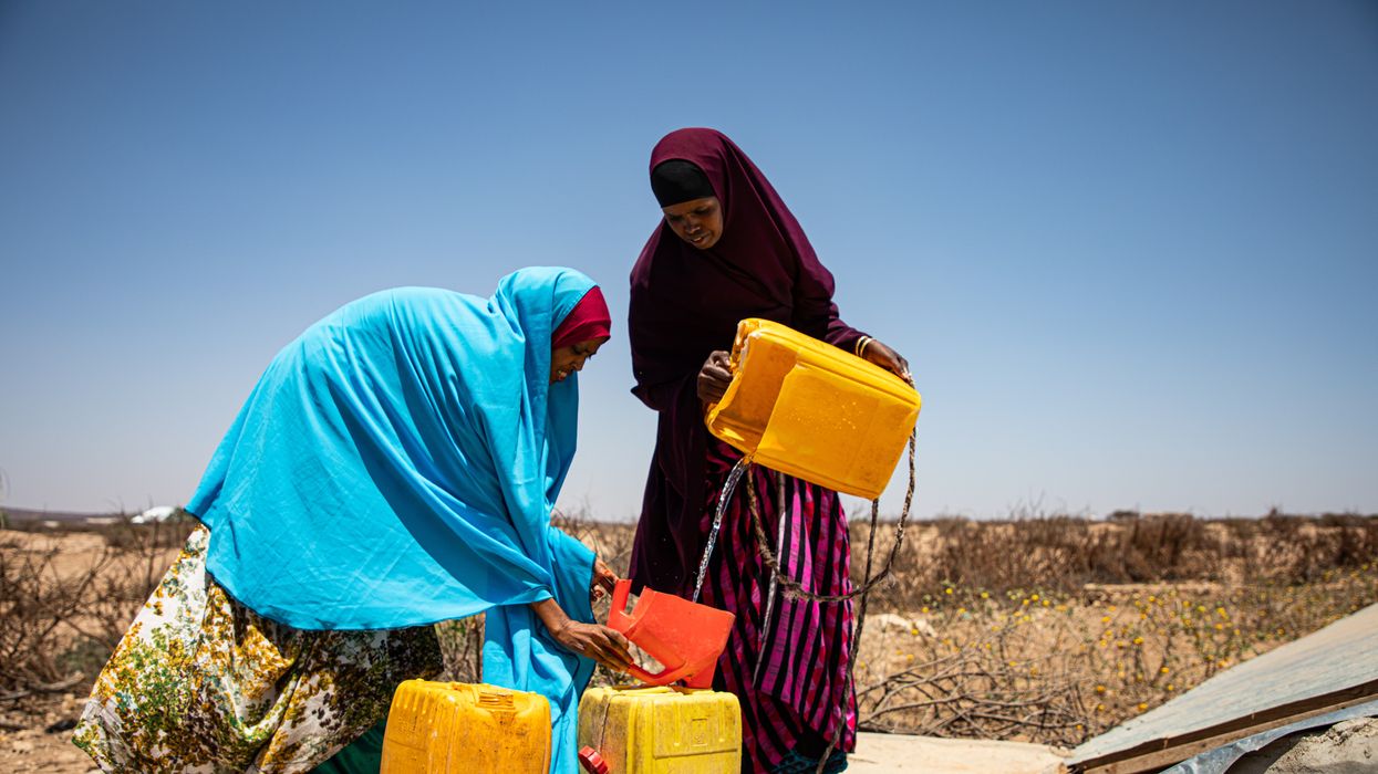 Two woman pour water from a yellow plastic tub.