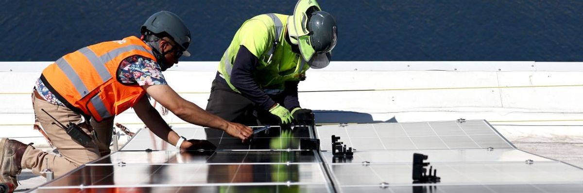 Two workers install rooftop solar panels. 