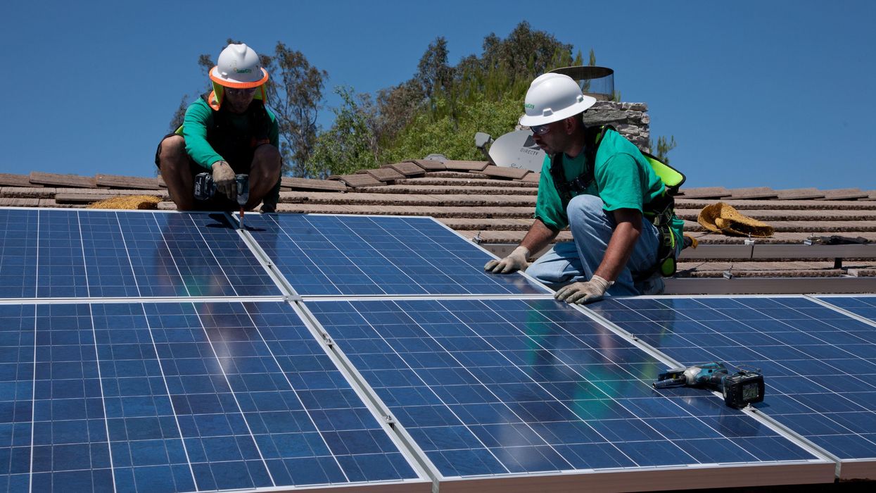 Two workers install solar panels on a home in Oak View, California.