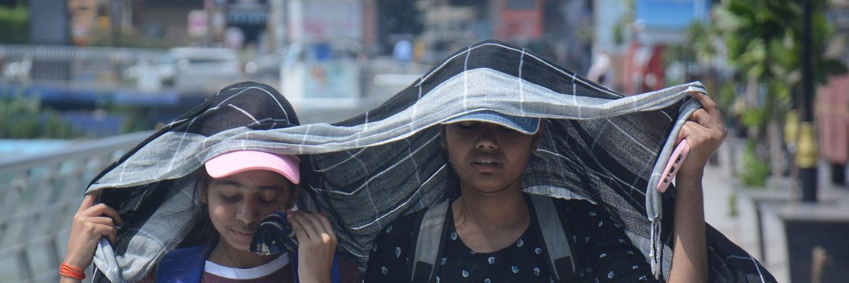 Two young girls cover their heads as they walk while drinking water in the scorching afternoon heat on April 25, 2022 in Mumbai, India. 