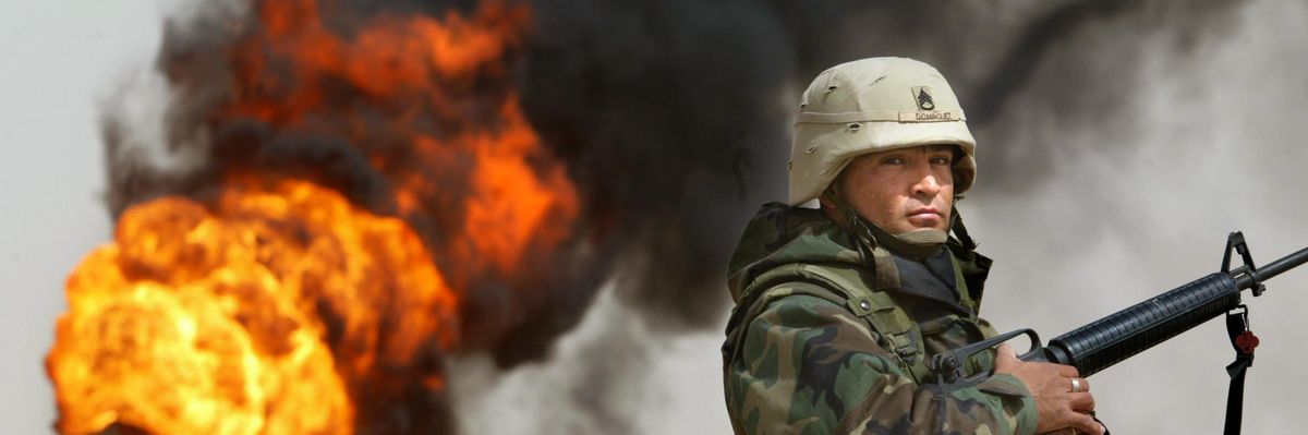 U.S. Army Staff Sergeant Robert Dominguez stands guard next to a burning oil well on March 27, 2003 in Rumayla, Iraq.