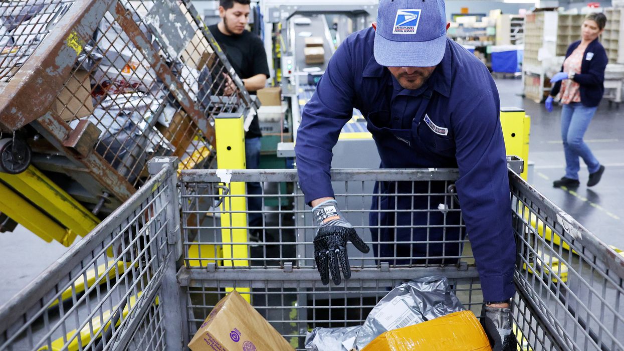 U.S. Postal Service employees place packages into a sorting machine