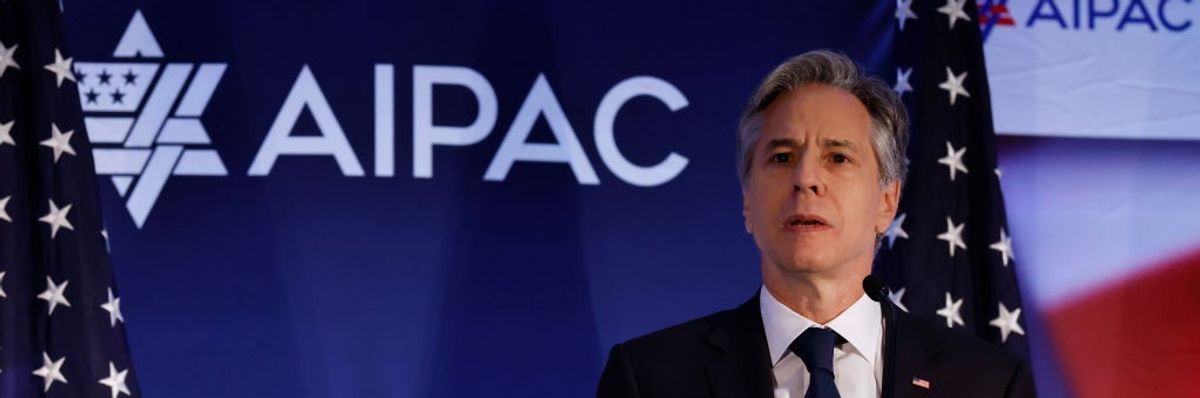 U.S. Secretary of State Antony Blinken stands in front of a blue background with AIPAC written on it.
