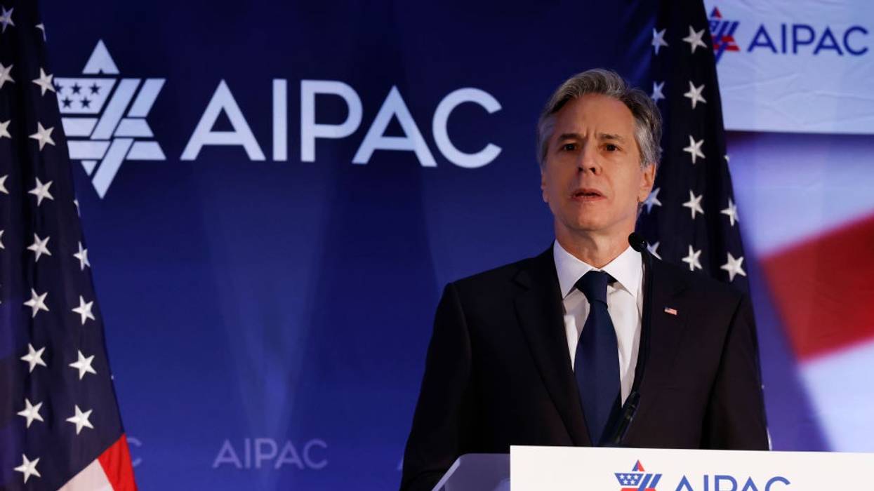 U.S. Secretary of State Antony Blinken stands in front of a blue background with AIPAC written on it.