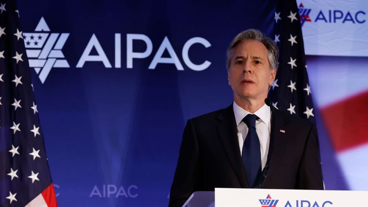 U.S. Secretary of State Antony Blinken stands in front of a blue background with AIPAC written on it.