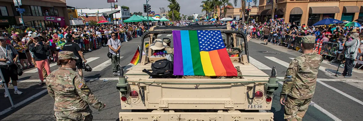 U.S. soldiers march in parade with rainbow American flag.