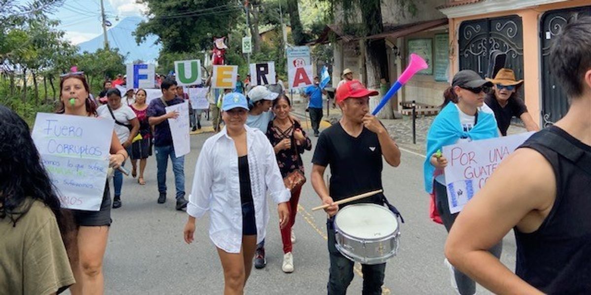 \u200bProtesters march down a street with drums.