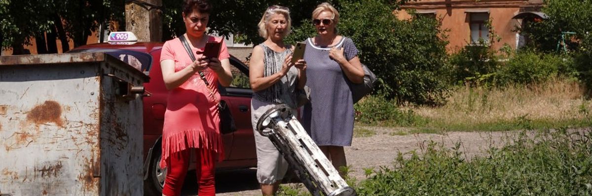 Ukrainian women photograph the remnants of a cluster bomb