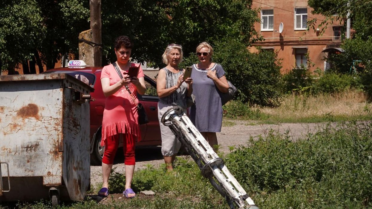Ukrainian women photograph the remnants of a cluster bomb