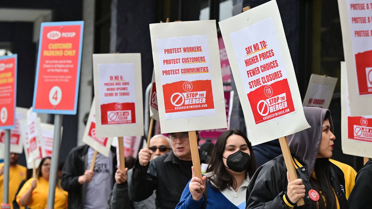 Unionized grocery store worker march with signs saying, "Stop the merger."