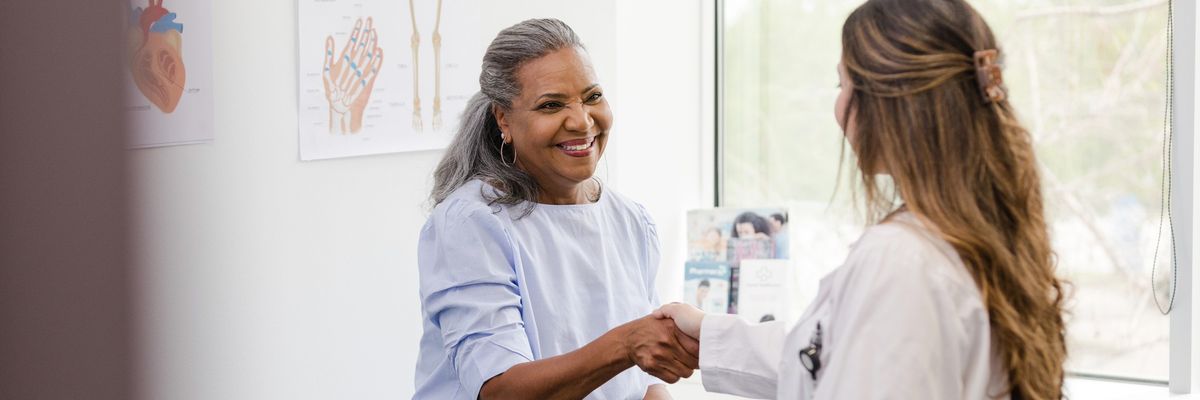 Unrecognizable doctor shakes hands with senior female patient