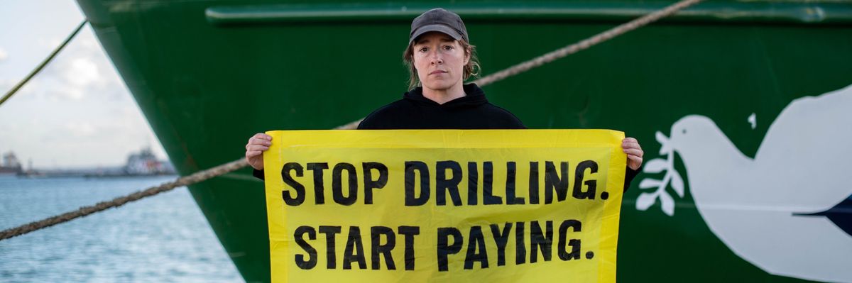 Usnea Granger, Greenpeace activist, holding a sign that reads: "Stop Drilling. Start Paying."