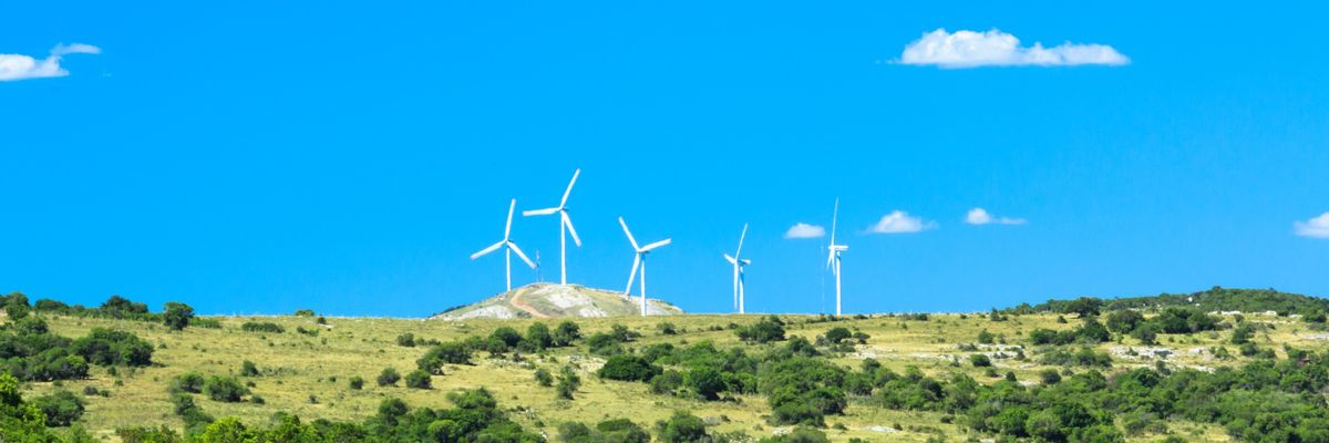 Windmills on a green hill against a blue sky.