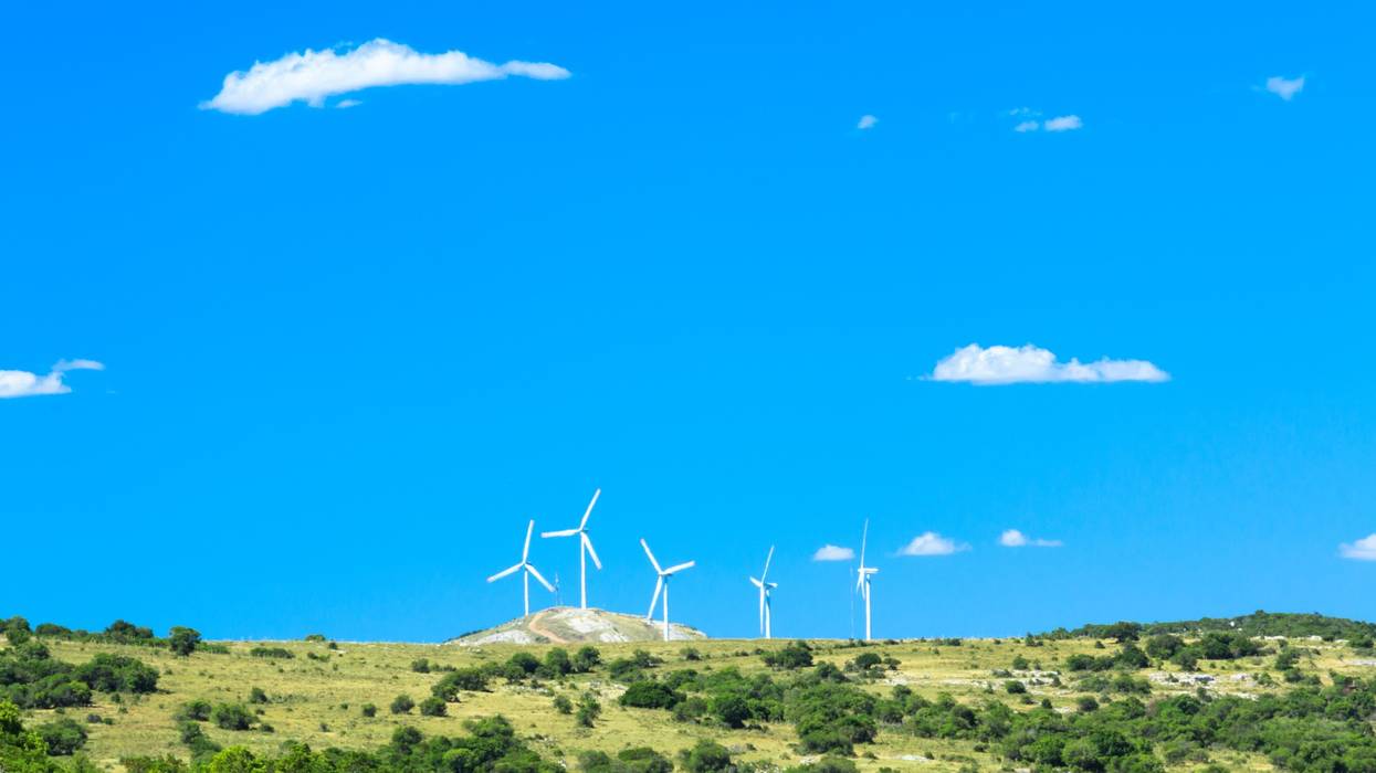 Windmills on a green hill against a blue sky.