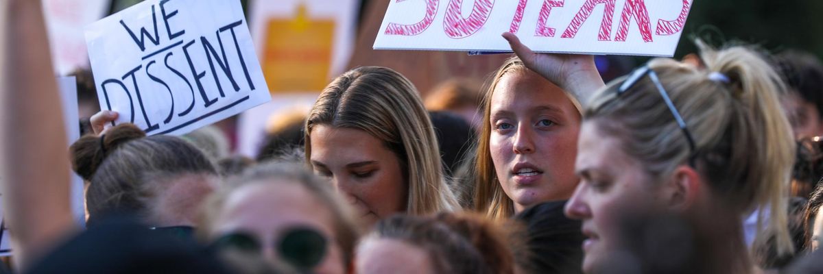 Woman holding a sign that says "Don't forget to turn the clocks back 50 years."