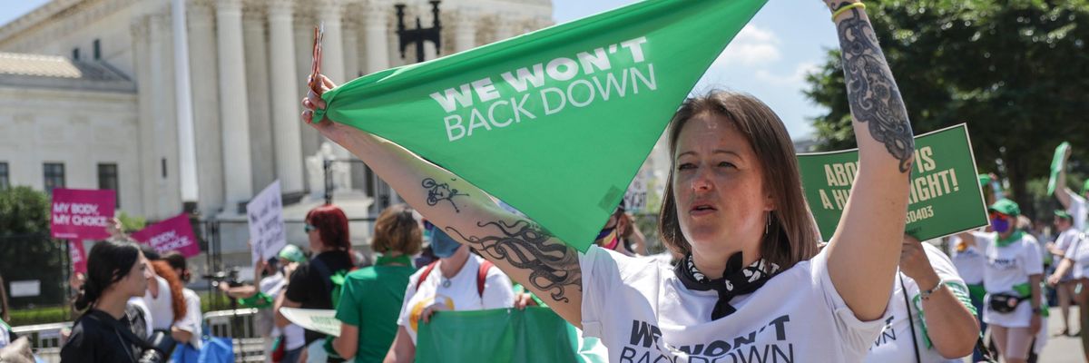 Woman holds banner reading, "We won't back down" outside Supreme Court