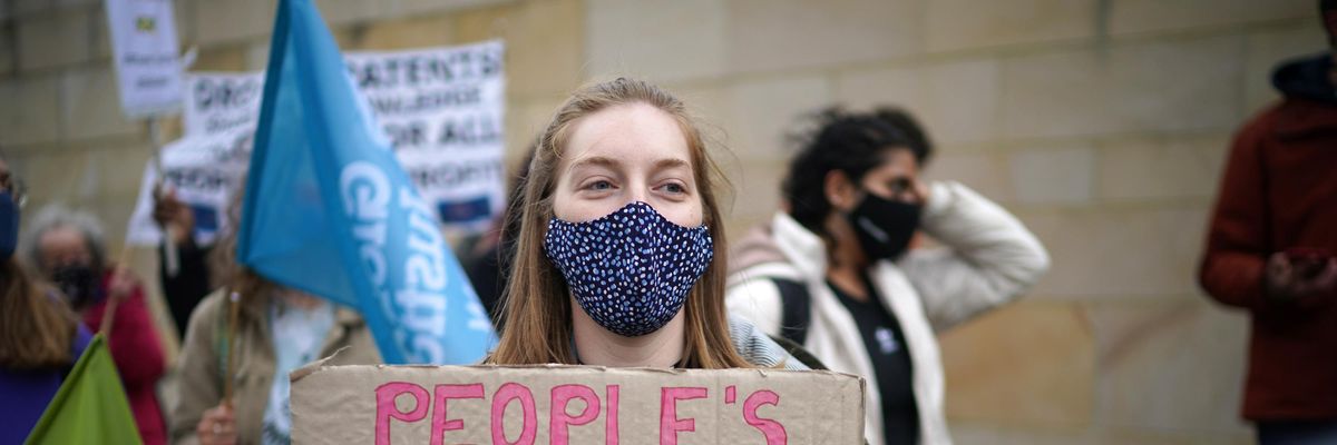 Woman holds sign reading, "people's vaccine not profit vaccine"