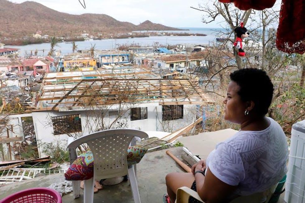 Woman looks away from camera at damaged buildings by the sea.