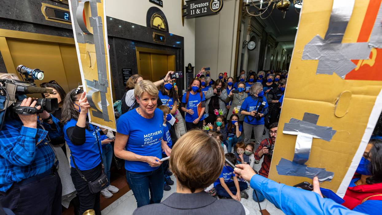 Women and children in blue shirts speak to a woman in a gray suit.