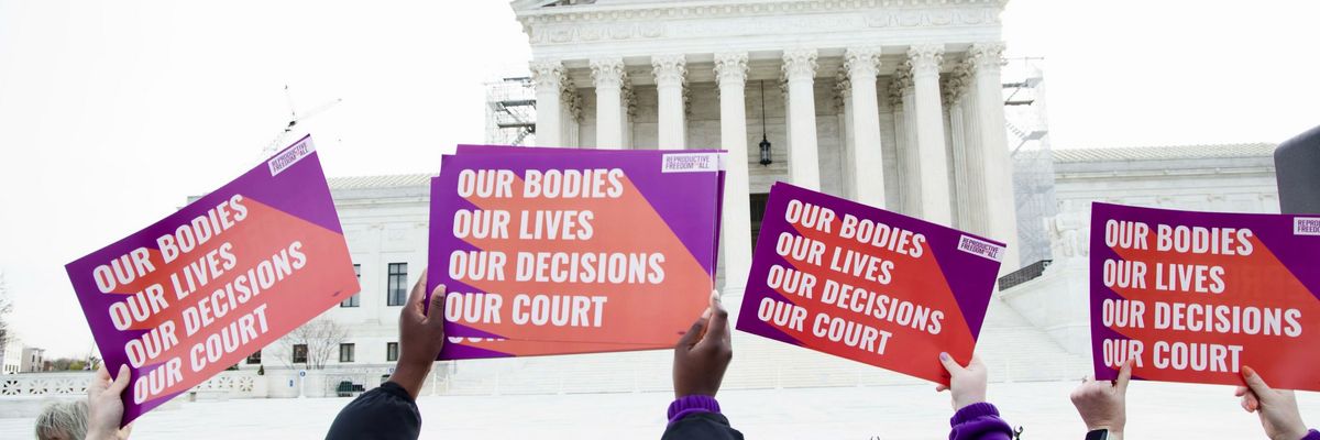 Women hold up signs reading "our bodies, our lives, our decisions, our court" outside the Supreme Court