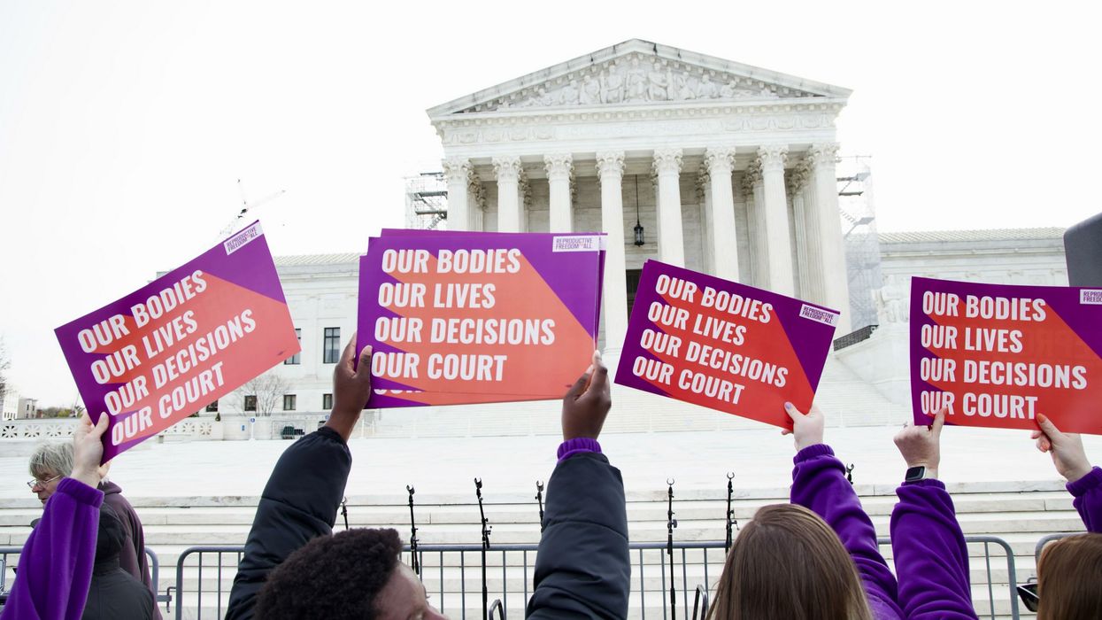 Women hold up signs reading "our bodies, our lives, our decisions, our court" outside the Supreme Court