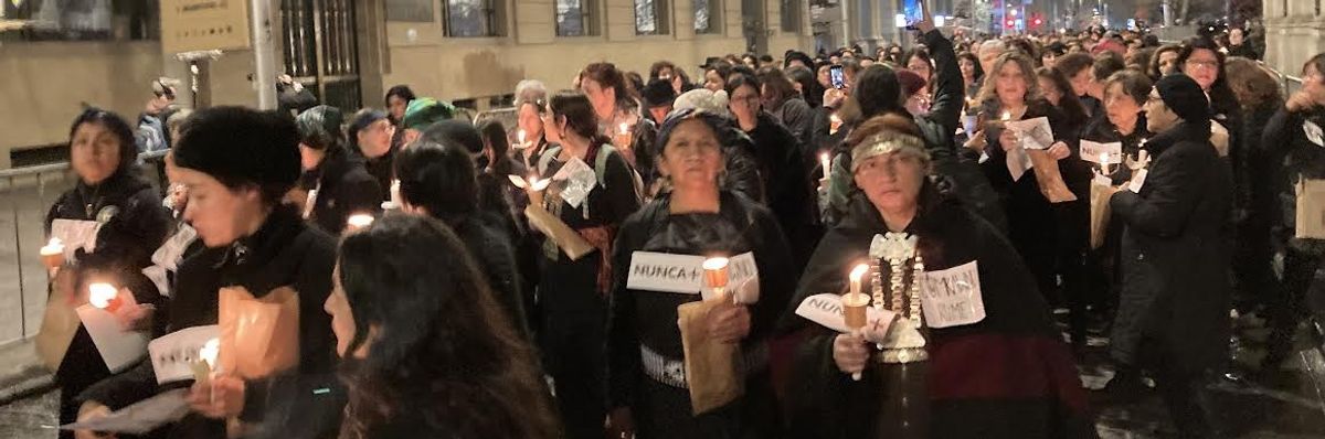Women march in black carrying candles and signs reading, "Nunca." 