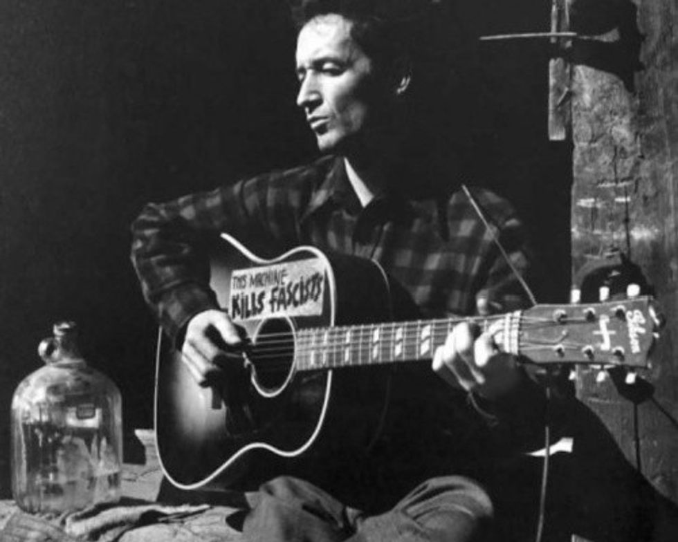 Woody Guthrie performs with his "This Machine Kills Fascists" guitar. 