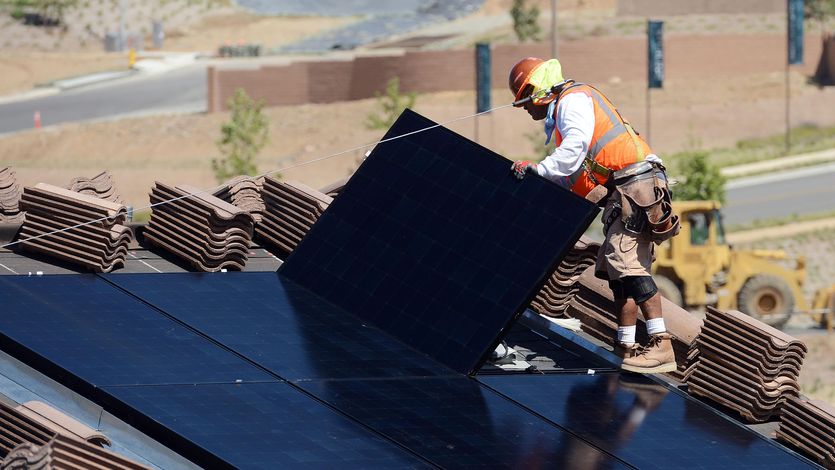 Workers install solar panels on the roofs of homes
