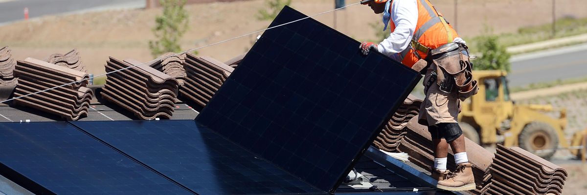 Workers install solar panels on the roofs of homes