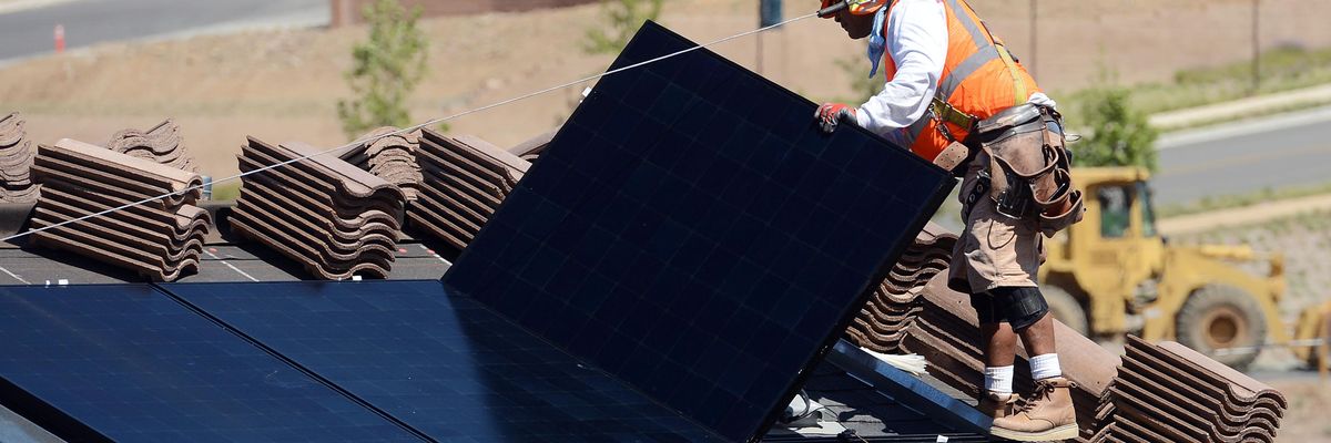 Workers install solar panels on the roofs of homes