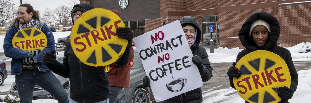 Workers stand in the snow with signs protesting Starbucks.