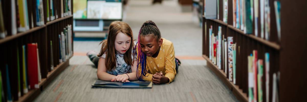 young girls laying on floor reading a picture book