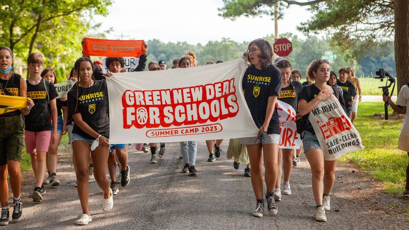 ​Young organizers hold up a banner celebrating the "Green New Deal for Schools Summer Camp 2023."