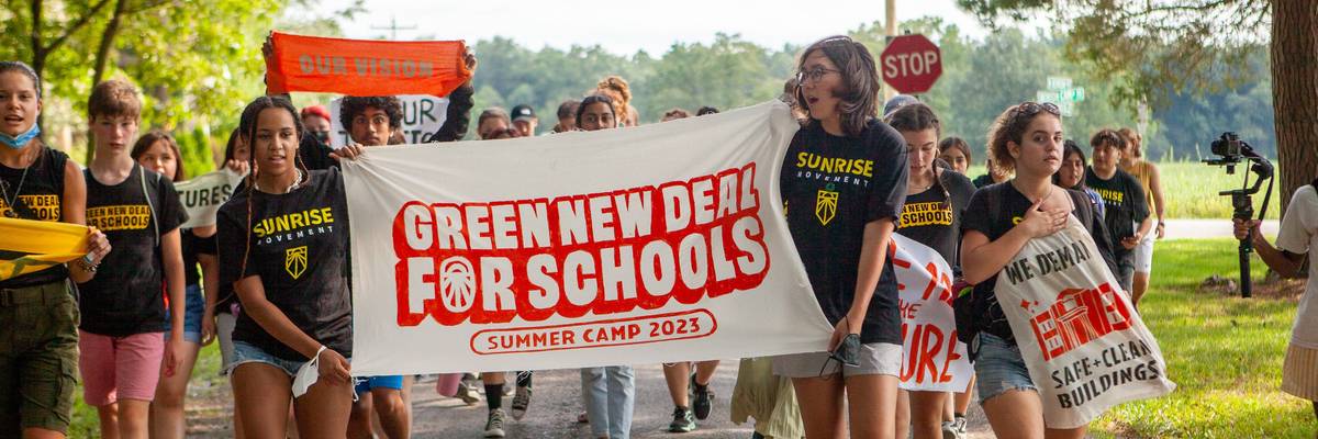 Young organizers hold up a banner celebrating the "Green New Deal for Schools Summer Camp 2023."