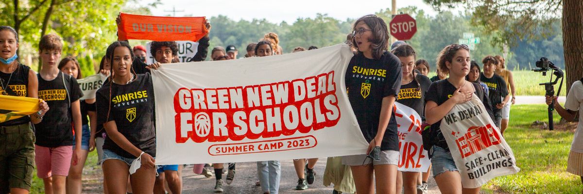 Young organizers hold up a banner celebrating the "Green New Deal for Schools Summer Camp 2023."