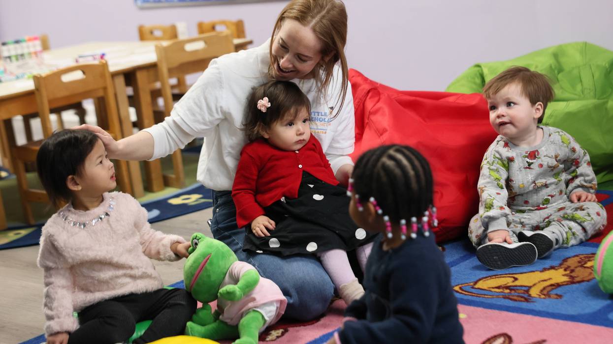 Young students from Little Scholars sit on a rug with a teacher.