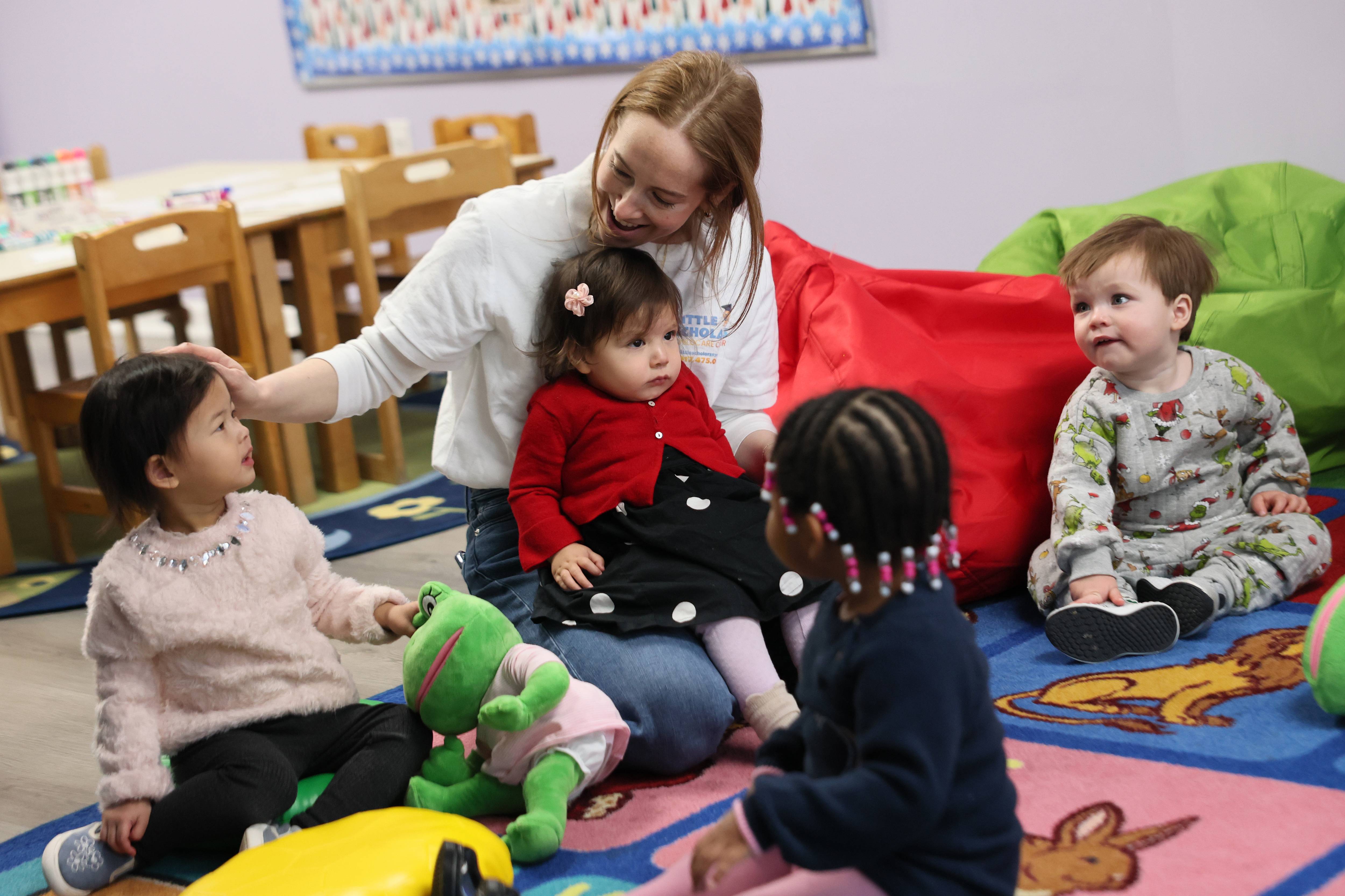 Young students from Little Scholars sit on a rug with a teacher.