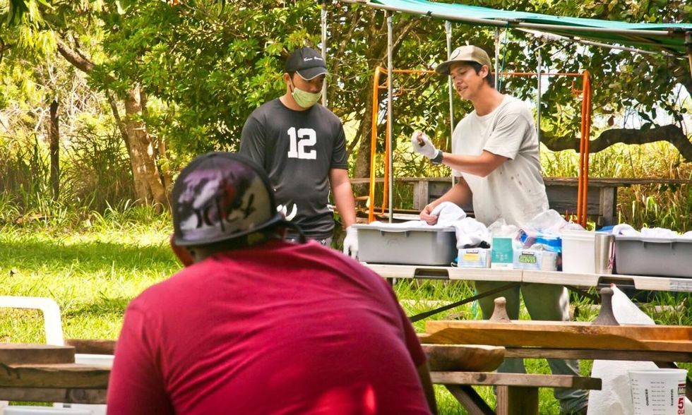 Youth mentor Loa Patao, right, demonstrates how to clean boiled kalo before pounding it to make the Hawaiian food staple poi. (Photo: Malia Welch)