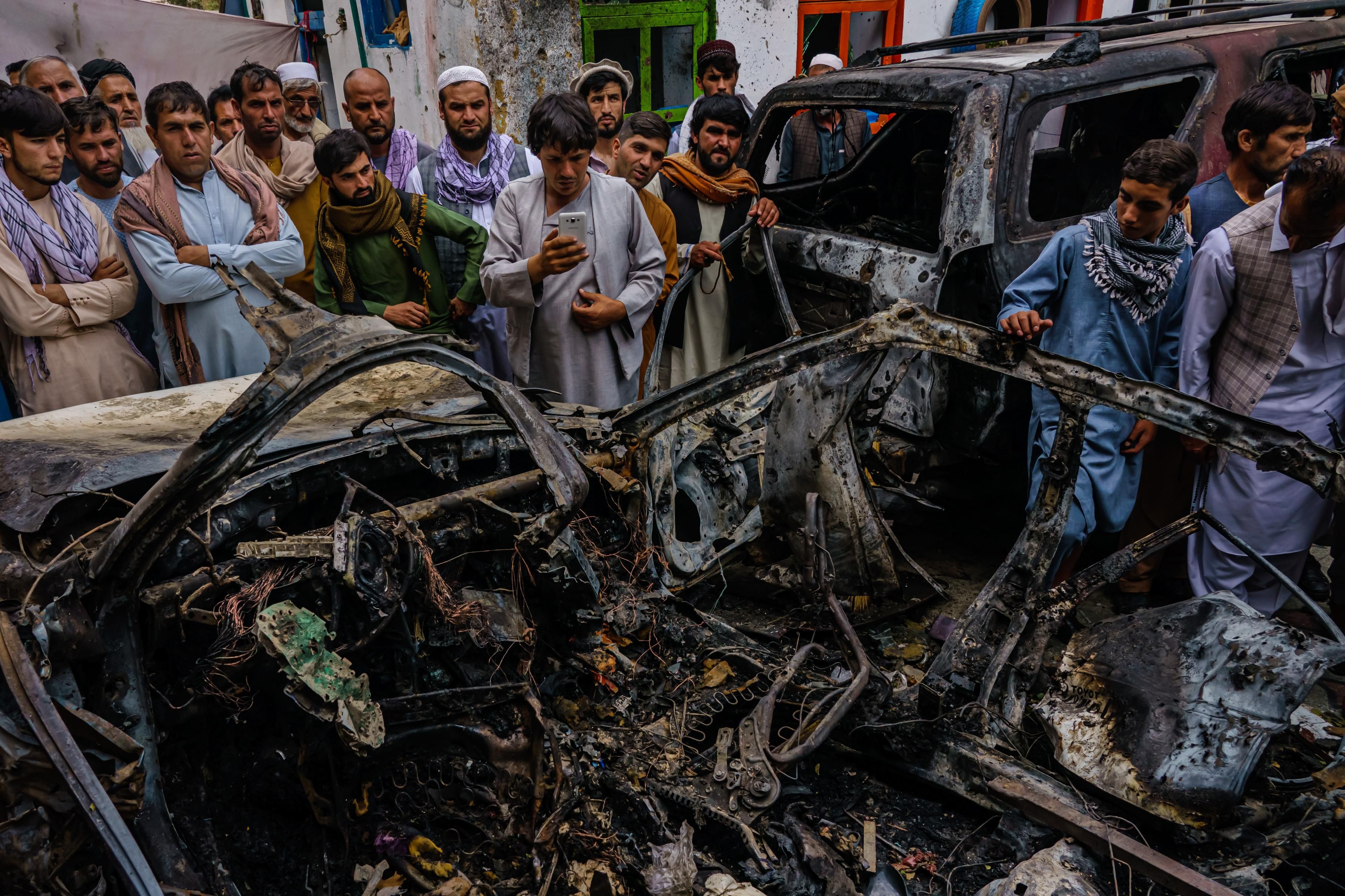 Afghans gather around a car incinerated by a U.S. drone strike
