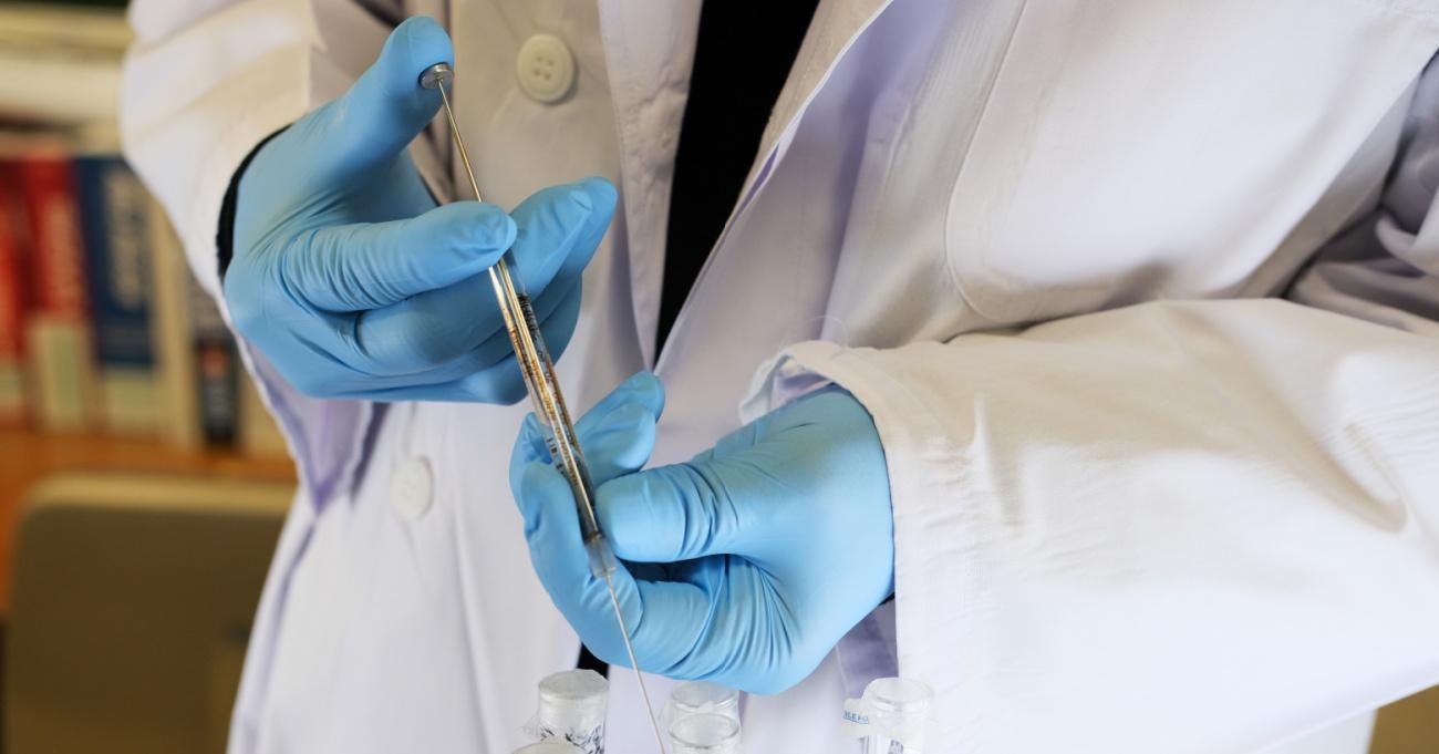 A researcher holds a syringe over test vials. 