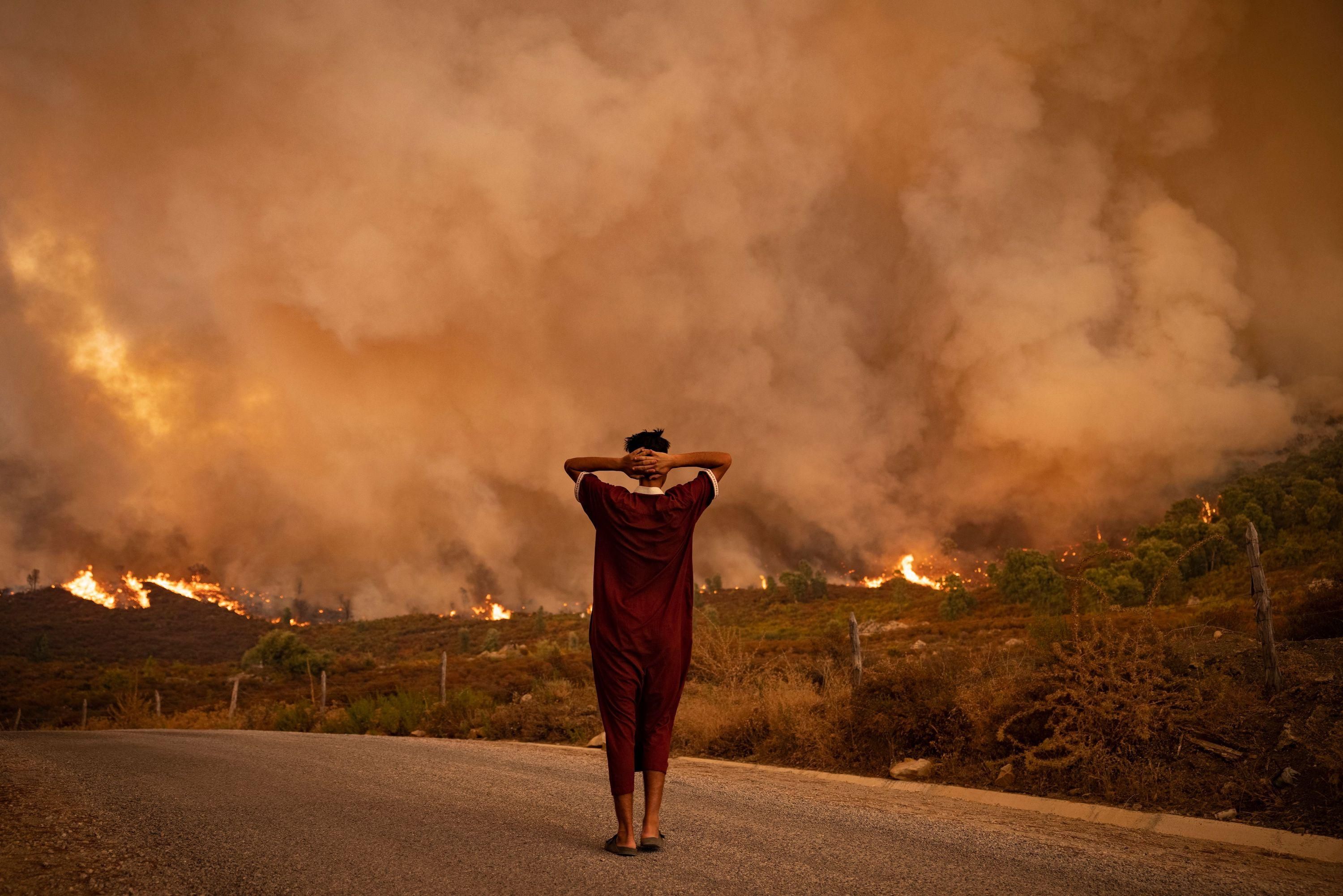 A woman looks at wildfires tearing through a forest in the region of Chefchaouen in northern Morocco on August 15, 2021.
