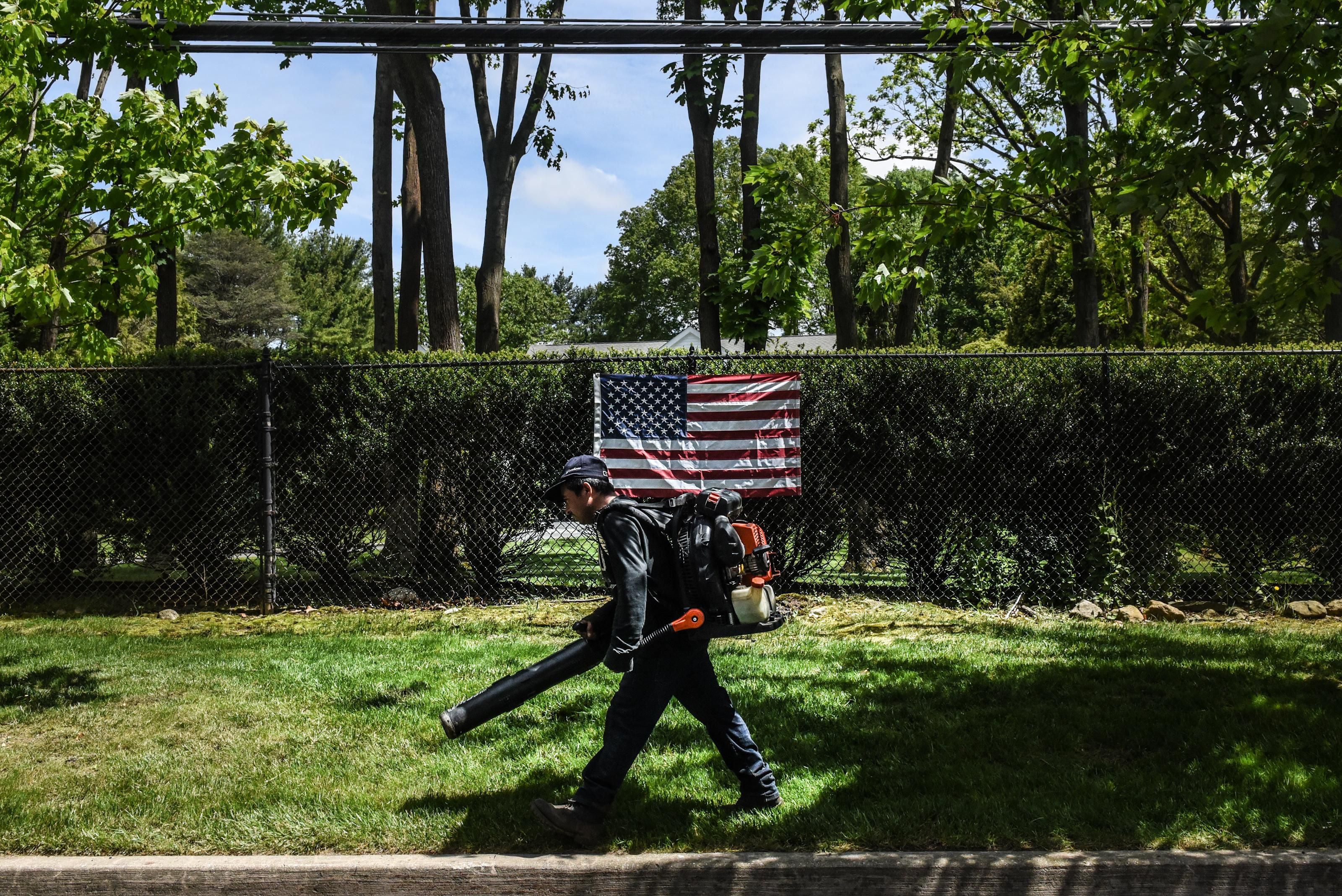  A person working as a leaf blower walks past an American flag on May 27, 2020 in Old Westbury, New York. (Photo by Stephanie Keith/Getty Images)