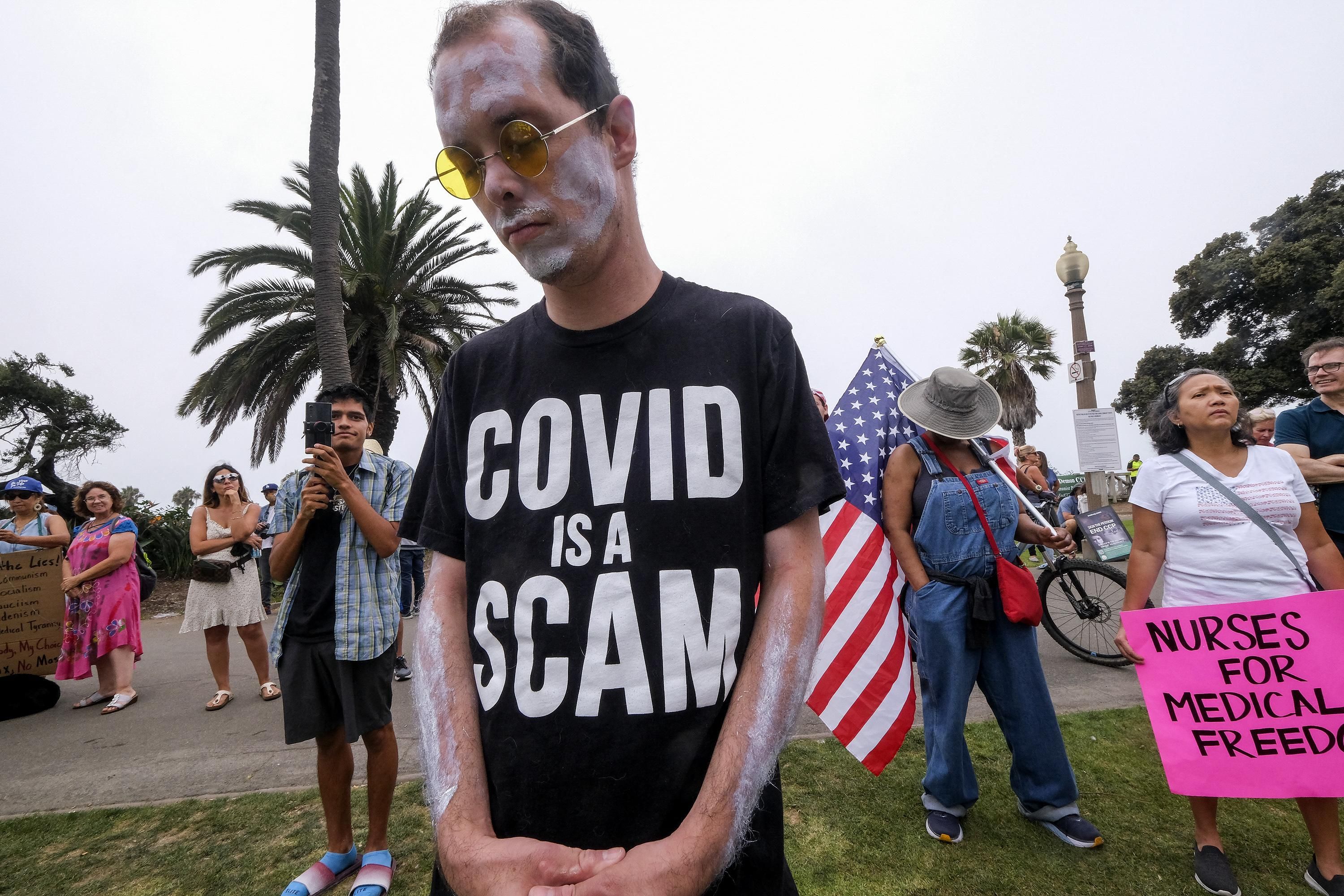 A man wears a shirt saying "Covid is a scam"